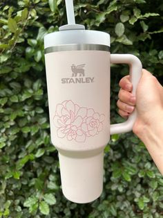 a hand holding a white coffee cup with a straw in it's mouth and the words stanley printed on it