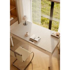 a desk with a book and chair in front of a window overlooking a grassy field