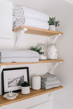 shelves with folded towels and other items on them in a white bathroom, along with a framed photograph