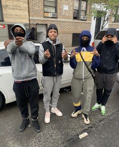 four people standing in front of a white car wearing hoodies and holding umbrellas