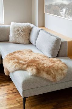 a couch with pillows on top of it in front of a window and wooden floor