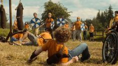 a group of men in orange shirts and blue shorts are playing with an old fashioned wheel chair