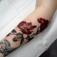 a woman's arm with red flowers on it and leaves around the wrist area