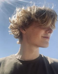 a close up of a person with long hair and sun shining in the sky behind him