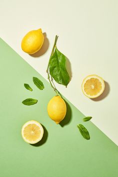 three lemons and two leaves on a green and white background with one cut in half