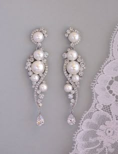 two pairs of white pearls and crystal earrings on a lace doily next to a pair of diamond - encrusted bridals