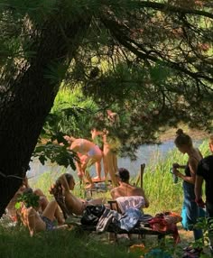 some people are sitting in the grass by a river and trees with their backs turned to one another