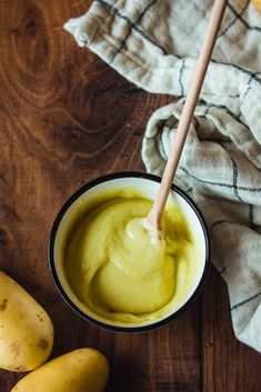 a wooden spoon in a bowl filled with green liquid next to bananas on a table