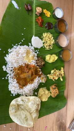 a banana leaf with different types of food on it and sauces next to it