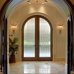 an arched doorway leads into a foyer with marble flooring and large glass doors that lead to the outside