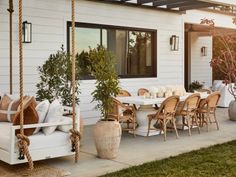 a porch with chairs, table and potted plants on the outside patio area in front of a white house