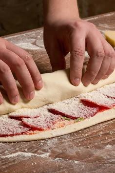 a person kneading dough on top of a wooden table next to a pizza