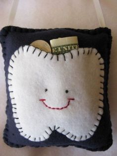 a tooth shaped pillow with a smile on it's face and a dollar bill sticking out of its mouth