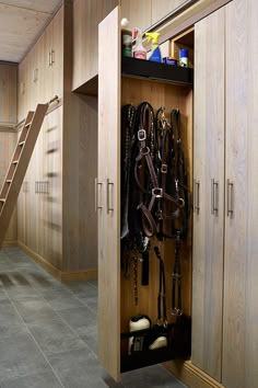 an open wooden closet with horse tacks and other items in it, next to a stair case