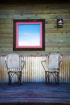 two chairs sitting next to each other in front of a wooden wall with a window