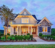 a house that is lit up at night with lights on and bushes in front of it