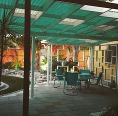 a covered patio with blue chairs and green table in the middle, surrounded by trees