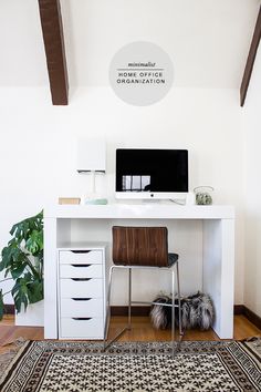 a white desk with a computer on top of it next to a rug and potted plant