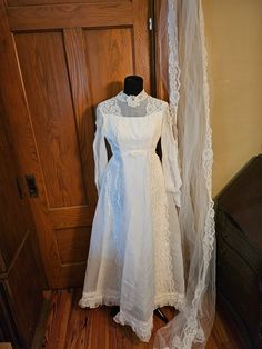 a white wedding dress on display in front of a wooden door with a veil hanging from it