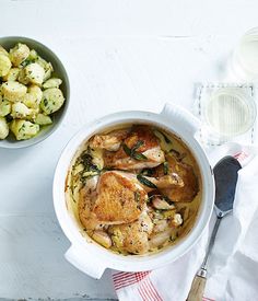 a bowl of chicken and potatoes next to a glass of water on a white table