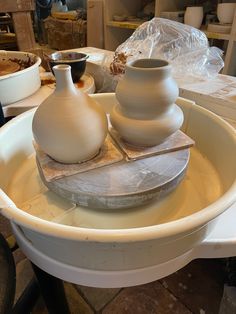 two white vases sitting on top of a table next to other bowls and containers