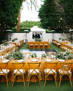 an outdoor wedding reception setup with yellow linens and greenery at the head table