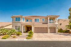 a large house with two car garages and palm trees on the side of the road