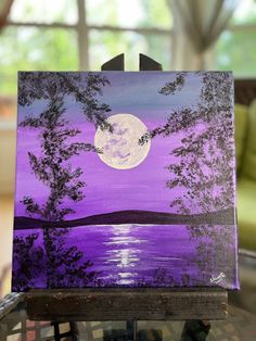 an easel with a painting on it that has a full moon in the background