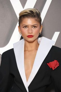 a woman wearing a black and white suit with red accents on her lapel, posing for the camera