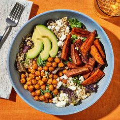 a blue bowl filled with lots of food next to a fork and knife on top of a table