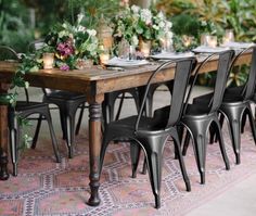 a long table with black chairs and white flowers on it is surrounded by greenery