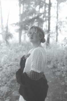 a woman standing in the woods with her hands on her hips and looking off to the side