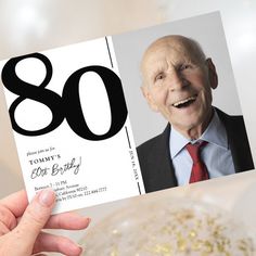 an old man holding up a birthday card with the number 80 on it and gold confetti in front of him