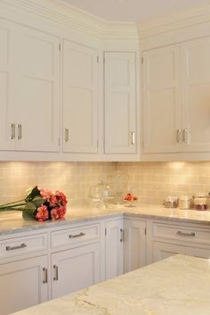 a kitchen with white cabinets and marble counter tops, flowers on the island top in front of the sink