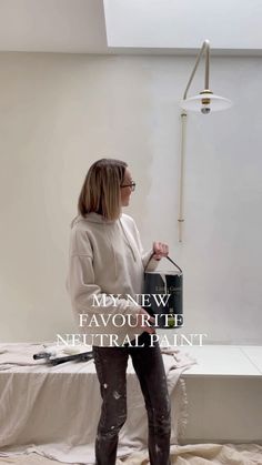 a woman standing on top of a bed in front of a white wall and holding a paint can