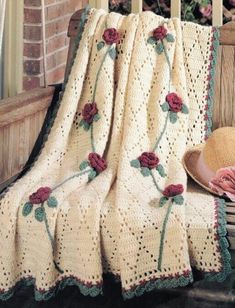 a crocheted blanket with roses on it and a hat sitting on a bench