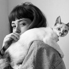 a black and white photo of a woman with a cat on her shoulders, looking at the camera