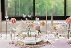 the table is set with pink and white flowers in vases, candles, and napkins