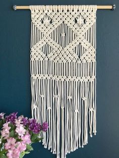 a white macrame hanging on a wall next to purple flowers