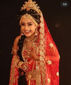 a woman in a red and gold bridal outfit posing for the camera with her hands on her hips