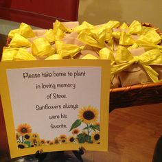 a basket full of sunflowers sitting on top of a table next to a sign that says please take home to plant in loving memory of steve