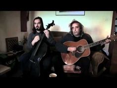 two men sitting on a couch playing guitars