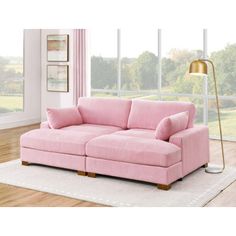 a pink couch sitting on top of a wooden floor next to a lamp and window