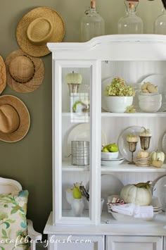 a white china cabinet filled with dishes and hats