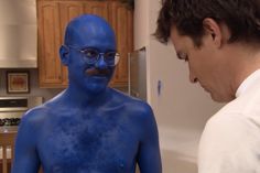 a man with blue paint on his body and glasses looking at another man's face