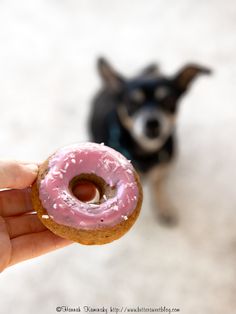 a person holding a doughnut with pink icing on it and a dog standing behind them