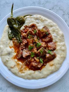 a white plate topped with hummus and meat covered in gravy next to a green pepper