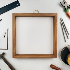 an empty wooden frame surrounded by tools and other kitchen utensils on a white surface