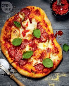 a pizza sitting on top of a wooden table next to pepperoni and basil leaves