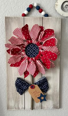 a red, white and blue flower is hanging on a wooden plaque with a tag